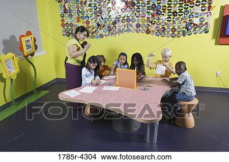 Picture - An art teacher observing her students drawing in art class. Fotosearch