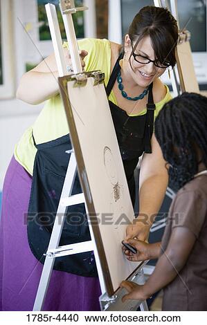 An art teacher showing young girl how to draw on an easel in art class View Large Photo Image Stock Image - An art teacher showing young girl how to draw on an easel in art class. Fotosearch