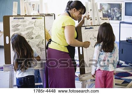 An art teacher showing young girls how to draw on an easel in art class View Large Photo Image Stock Photo - An art teacher showing young girls how to draw on an easel in art class. Fotosearch