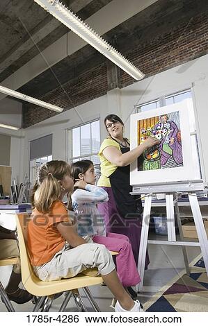 An art teacher standing by easel teaching her young students in art class View Large Photo Image Stock Photograph - An art teacher standing by easel teaching her young students in art class. Fotosearch