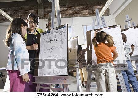 Picture - An art teacher with her student drawing on easels in art class. Fotosearch