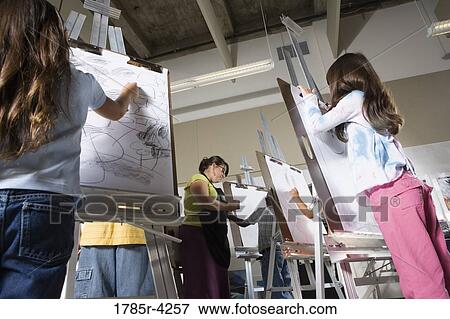 Stock Photo - An art teacher with her student drawing on easels in art class. Fotosearch