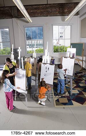 Stock Photo - An art teacher with her student drawing on easels in art class. Fotosearch