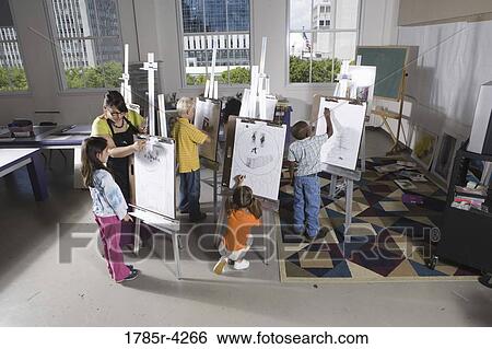 Stock Photograph - An art teacher with her student drawing on easels in art class. Fotosearch