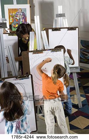 An art teacher with her students drawing on easels in art class View Large Photo Image Picture - An art teacher with her students drawing on easels in art class. Fotosearch
