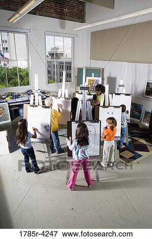 Stock Photo - An art teacher with her students drawing on easels in art class. Fotosearch