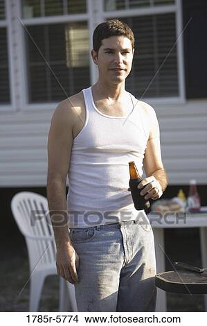 Blue-collar man holding drink bottle in front of trailer home View Large Photo Image Picture - Blue-collar man holding drink bottle in front of trailer home. Fotosearch