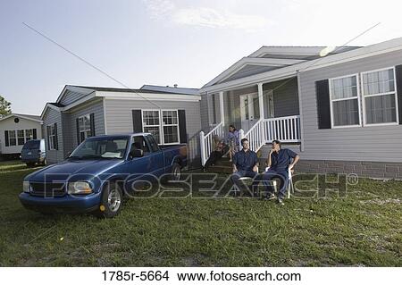 Picture - Blue-collar men sitting and talking in front yard of trailer home. Fotosearch
