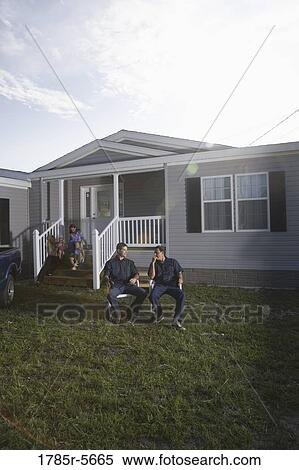 Stock Photography - Blue-collar men sitting and talking in front yard of trailer home. Fotosearch