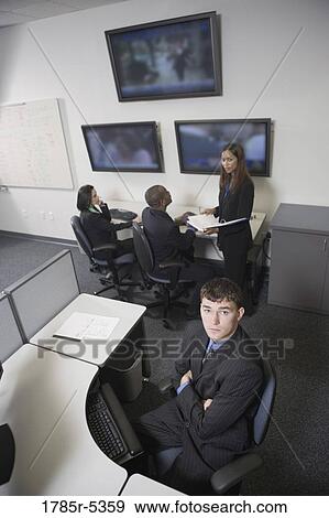 Stock Photo - Bored office worker at his desk with co-workers in the background. Fotosearch