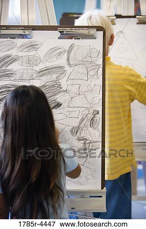 Boy and girl drawing on easels in art class View Large Photo Image Stock Photo - Boy and girl drawing on easels in art class. Fotosearch