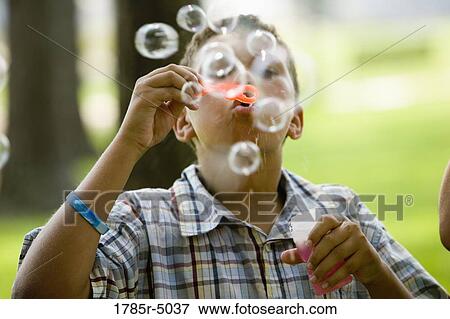 Boy blowing bubbles at a park View Large Photo Image Stock Photo - Boy blowing bubbles at a park. Fotosearch