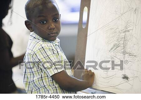 Boy drawing on easel in art class View Large Photo Image Stock Image - Boy drawing on easel in art class. Fotosearch
