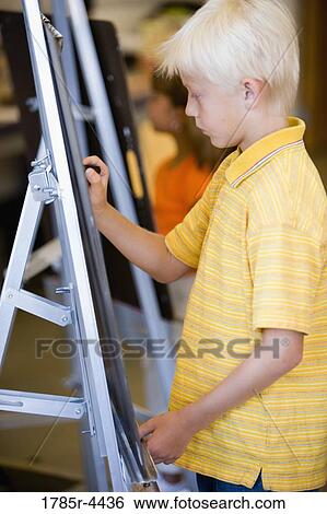 Boy drawing on easel in art class View Large Photo Image Stock Photograph - Boy drawing on easel in art class. Fotosearch