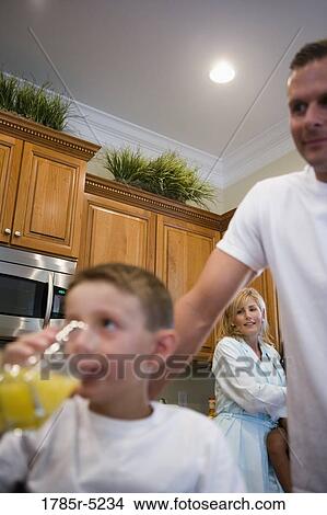 Boy drinking juice with father and mother in background View Large Photo Image Picture - Boy drinking juice with father and mother in background. Fotosearch