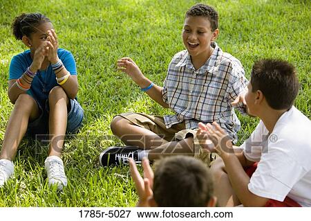 Boy telling stories to his friends while sitting on the grass at a park View Large Photo Image Stock Photo - Boy telling stories to his friends while sitting on the grass at a park. Fotosearch