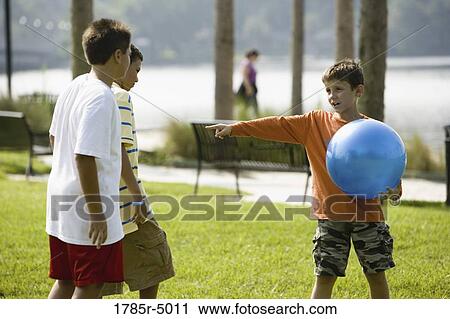 Stock Image - Boy with large blue ball playing with and giving instructions his friends. Fotosearch