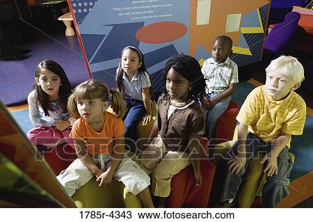 Stock Image - Boys and girls watching and listening attentively in a class. Fotosearch