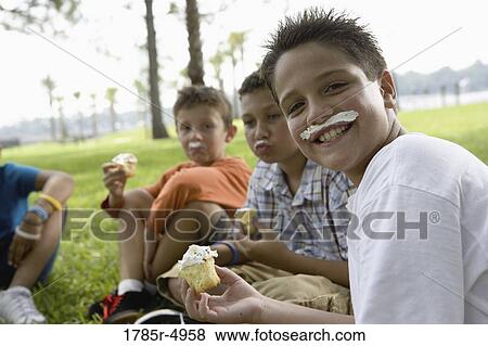 Boys eating cupcakes at a park View Large Photo Image Stock Photo - Boys eating cupcakes at a park. Fotosearch