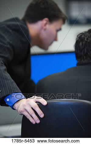 Business man with hand resting on back of chair leaning over computer monitor with colleague View Large Photo Image Stock Image - Business man with hand resting on back of chair leaning over computer monitor with colleague. Fotosearch