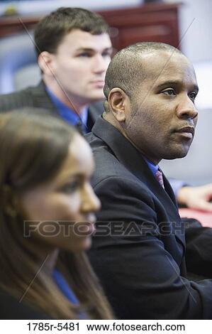 Business men and women watching and listening attentively in a meeting View Large Photo Image Stock Image - Business men and women watching and listening attentively in a meeting. Fotosearch