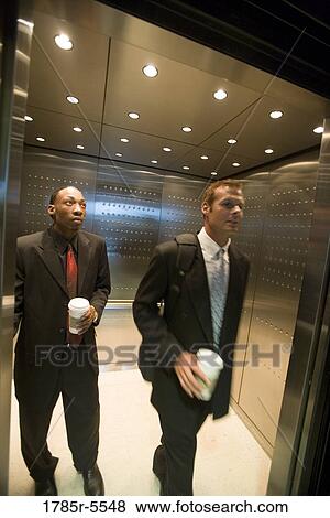 Stock Photo - Business people holding coffee cups exiting an elevator. Fotosearch
