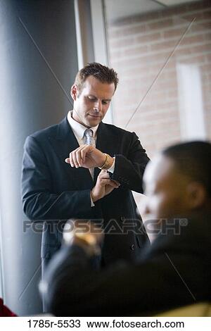 Stock Image - Business people sitting and waiting in an office lobby, looking at their watches. Fotosearch