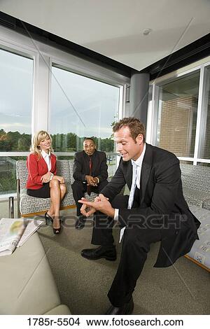 Business people sitting in an office lobby conversing amongst themselves View Large Photo Image Picture - Business people sitting in an office lobby conversing amongst themselves. Fotosearch