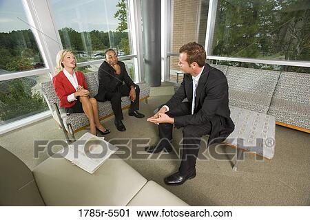 Stock Image - Business people sitting in an office lobby conversing amongst themselves. Fotosearch