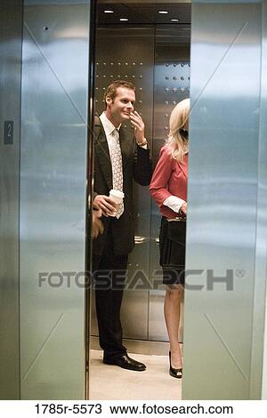 Stock Image - Business people standing in elevator with the doors closing. Fotosearch