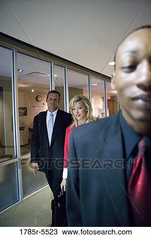 Stock Image - Business people walking down office hallway and lobby and conversing. Fotosearch
