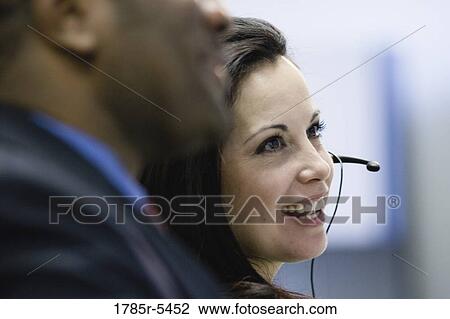 Stock Image - Business woman using headset with colleague in foreground. Fotosearch