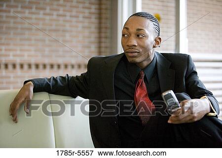Stock Photo - Businessman holding mobile phone while sitting in an office lobby. Fotosearch