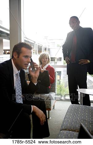 Businessman on cell phone while his colleagues watch in the background View Large Photo Image Picture - Businessman on cell phone while his colleagues watch in the background. Fotosearch