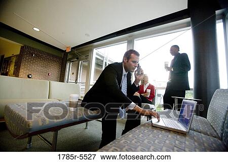 Stock Photo - Businessman on cell phone while his colleagues have coffee in the background. Fotosearch