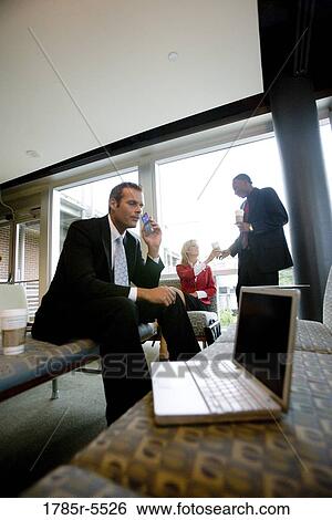 Businessman on cell phone while his colleagues have coffee in the background View Large Photo Image Stock Photograph - Businessman on cell phone while his colleagues have coffee in the background. Fotosearch