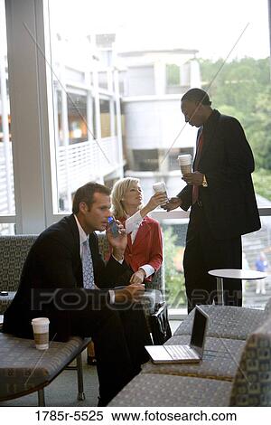 Businessman on cell phone while his colleagues have coffee in the background View Large Photo Image Stock Photography - Businessman on cell phone while his colleagues have coffee in the background. Fotosearch