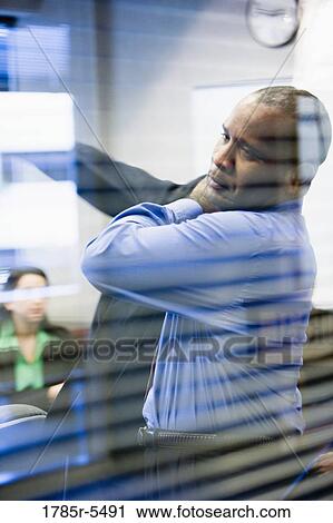 Stock Image - Businessman putting on his jacket viewed through conference room window. Fotosearch