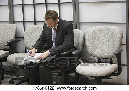 Stock Image - Businessman seated in an office writing in his folder. Fotosearch