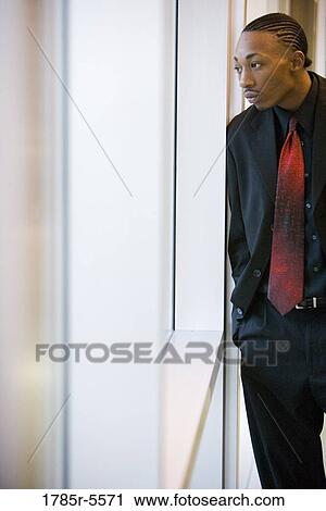 Stock Image - Businessman standing and leaning against a window. Fotosearch