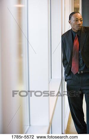 Stock Image - Businessman standing and leaning against a window. Fotosearch