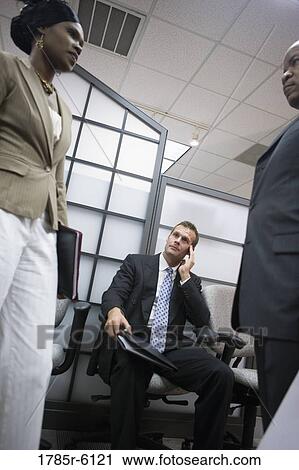 Stock Image - Businessman watching others talk. Fotosearch