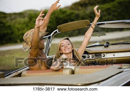 Cheerful and playful couple sitting and waving in antique convertible car View Large Photo Image Stock Photo - Cheerful and playful couple sitting and waving in antique convertible car. Fotosearch