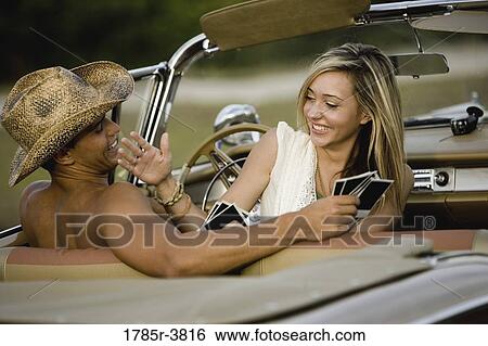 Stock Photograph - Cheerful and playful couple sitting in antique convertible car. Fotosearch