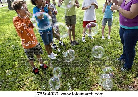 Children and their teacher blowing bubbles at a park View Large Photo Image Stock Image - Children and their teacher blowing bubbles at a park. Fotosearch