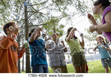 Children and their teacher blowing bubbles at a park View Large Photo Image Stock Photo - Children and their teacher blowing bubbles at a park. Fotosearch