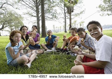 Children and their teacher sitting in a circle on the grass eating cupcakes View Large Photo Image Stock Photo - Children and their teacher sitting in a circle on the grass eating cupcakes. Fotosearch
