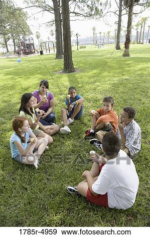 Children and their teacher sitting in a circle on the grass eating cupcakes View Large Photo Image Stock Photo - Children and their teacher sitting in a circle on the grass eating cupcakes. Fotosearch