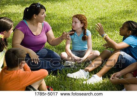 Stock Photo - Children and their teacher sitting in a circle on the grass at a park. Fotosearch