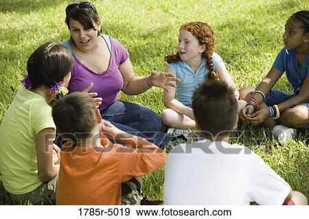 Children and their teacher sitting in a circle on the grass at a park View Large Photo Image Stock Photo - Children and their teacher sitting in a circle on the grass at a park. Fotosearch